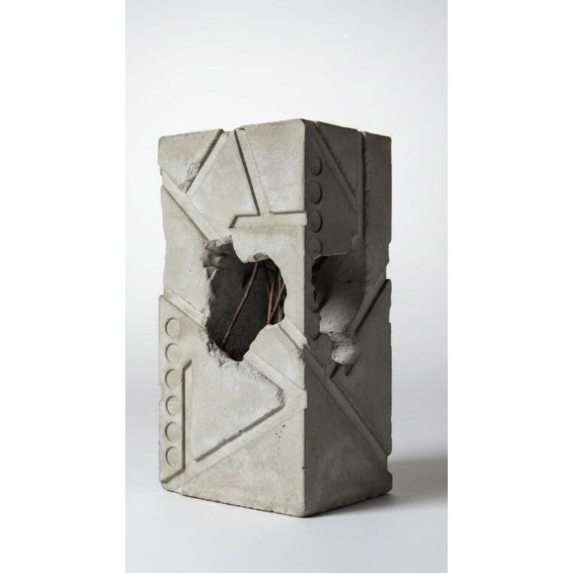 Concrete block with a large hole in it on a concrete surface with trees in the background.